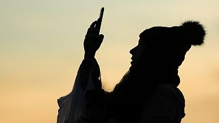 Силуэт человека на вечернем фоне неба делает фотографию на смартфоне в Филадельфии, четверг, 12 декабря 2019 года..