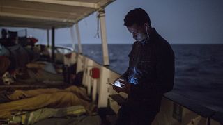 Мигрант вчера свой мобильный телефон, пока другие спят на палубе гуманитарного катера Open Arms испанской неправительственной организации Proactiva Open Arms, воскресенье, 1 июля 2018 года..